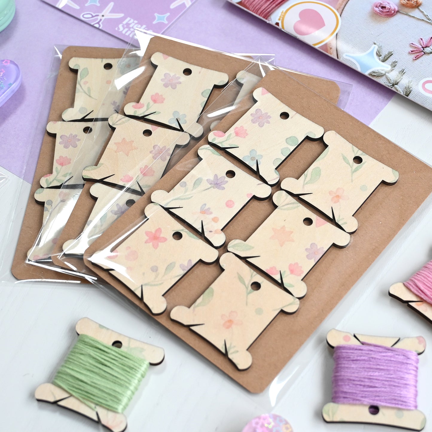 Set of wooden floss bobbins with floral designs on a cardboard backing, with spools of thread below.