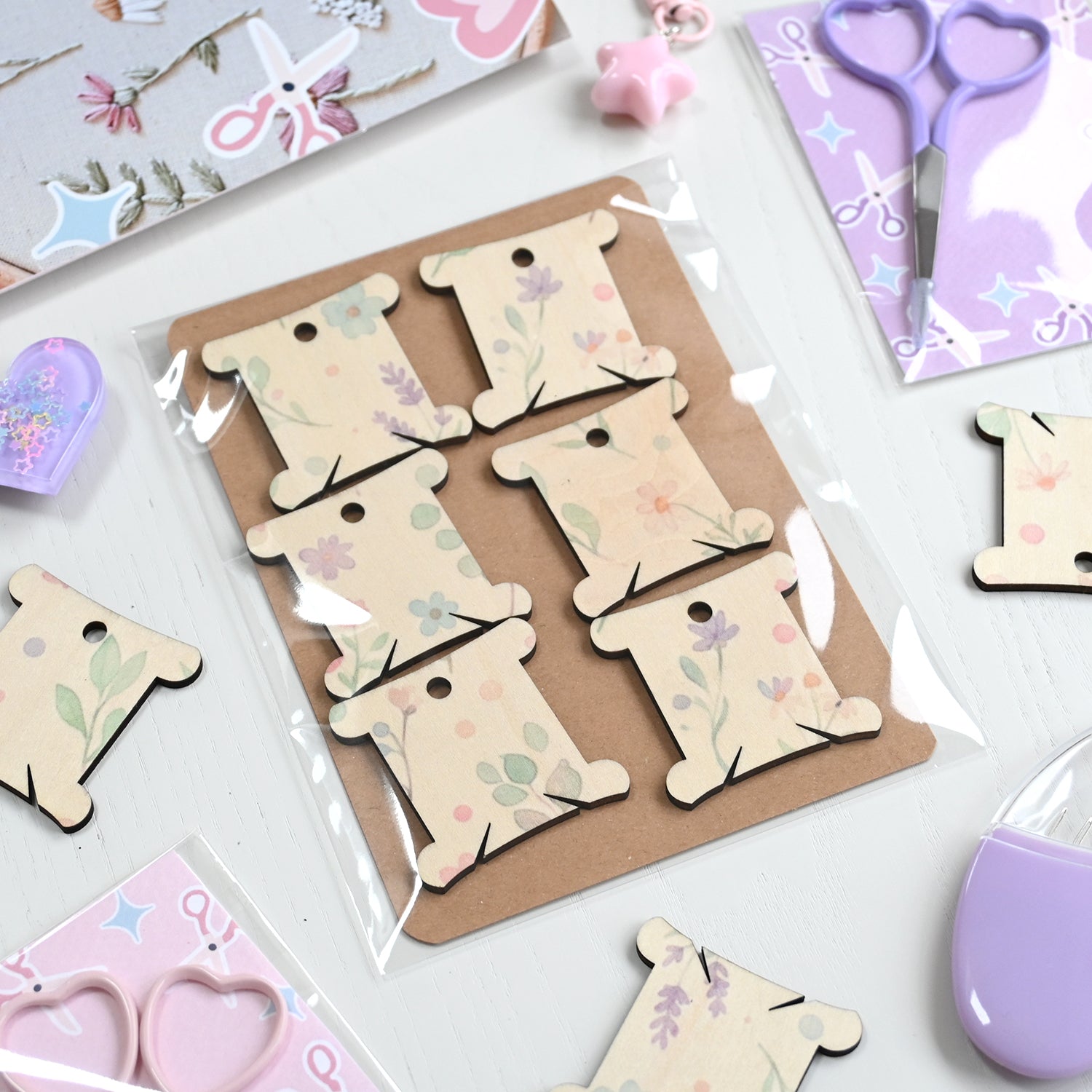 Set of wooden embroidery floss  tags with floral designs on a white surface with craft supplies.
