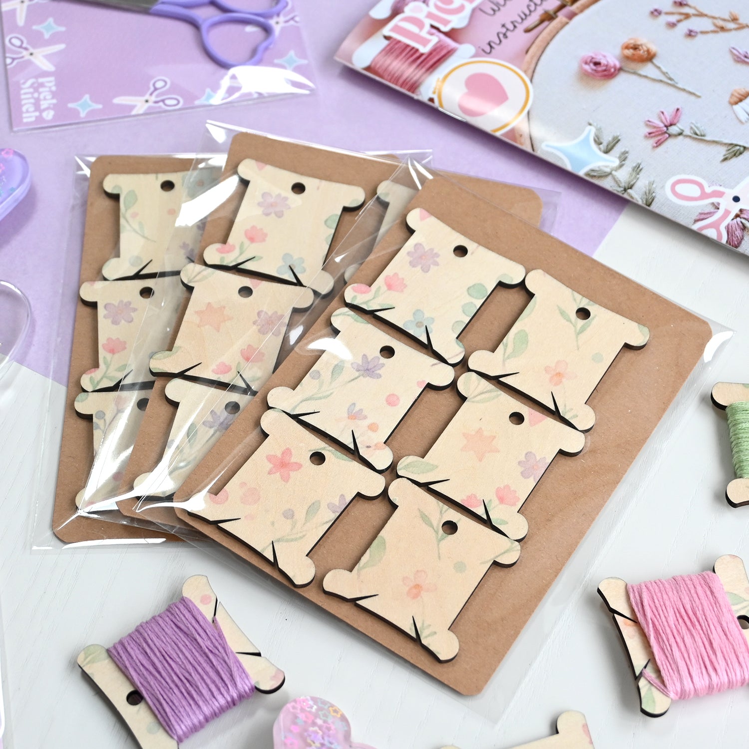 Set of wooden embroidery tags with floral patterns on a cardboard backing, surrounded by decorative embroidery items.