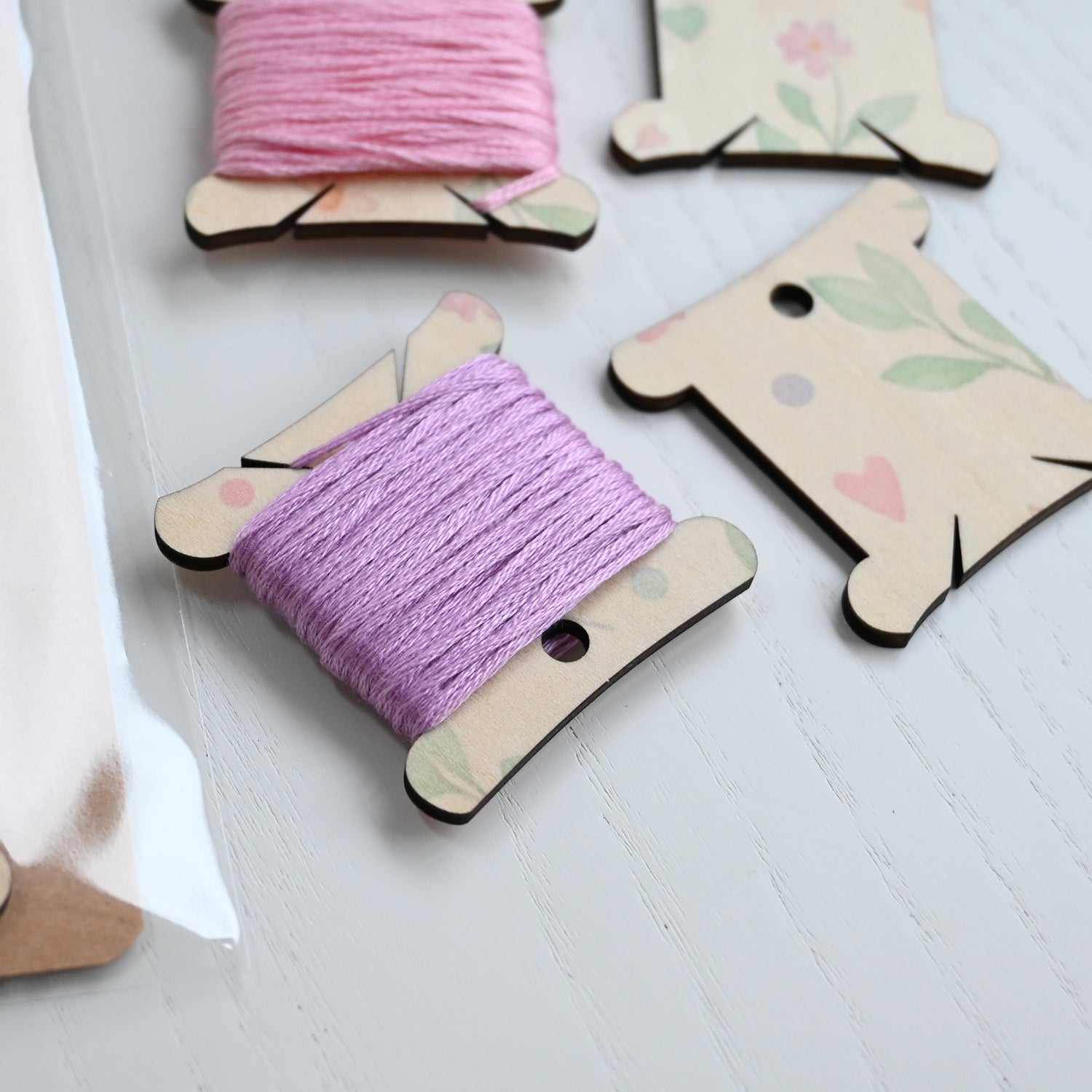Wooden thread spools with pink and purple thread on a light wooden surface