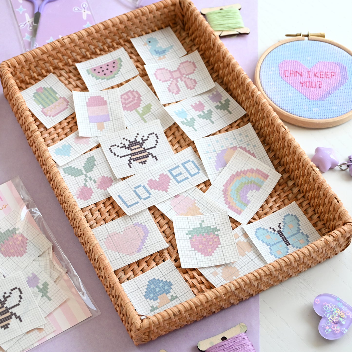 Basket of cross-stitch patterns with a embroidery hoop and thread in the background