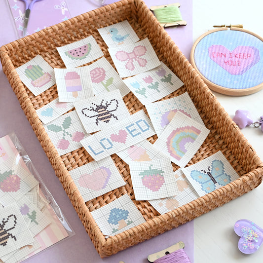 Basket of cross-stitch patterns with a embroidery hoop and thread in the background