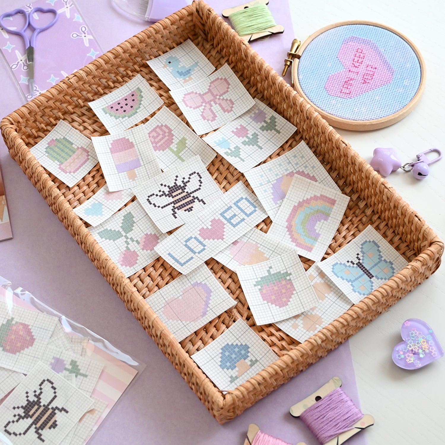 Basket of cross-stitching patterns on a table with embroidery hoop and thread spool.