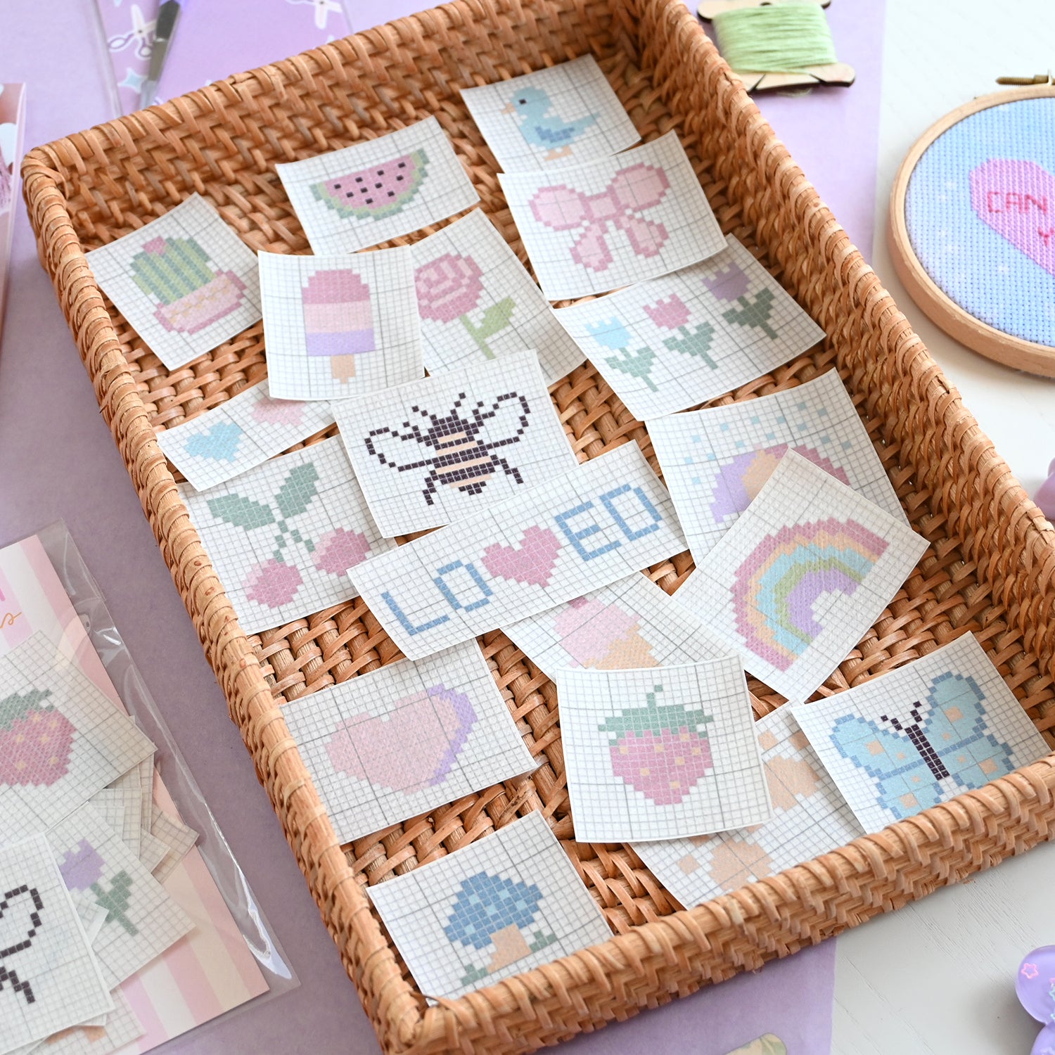 Cross-stitch patches in a woven basket on a light purple surface