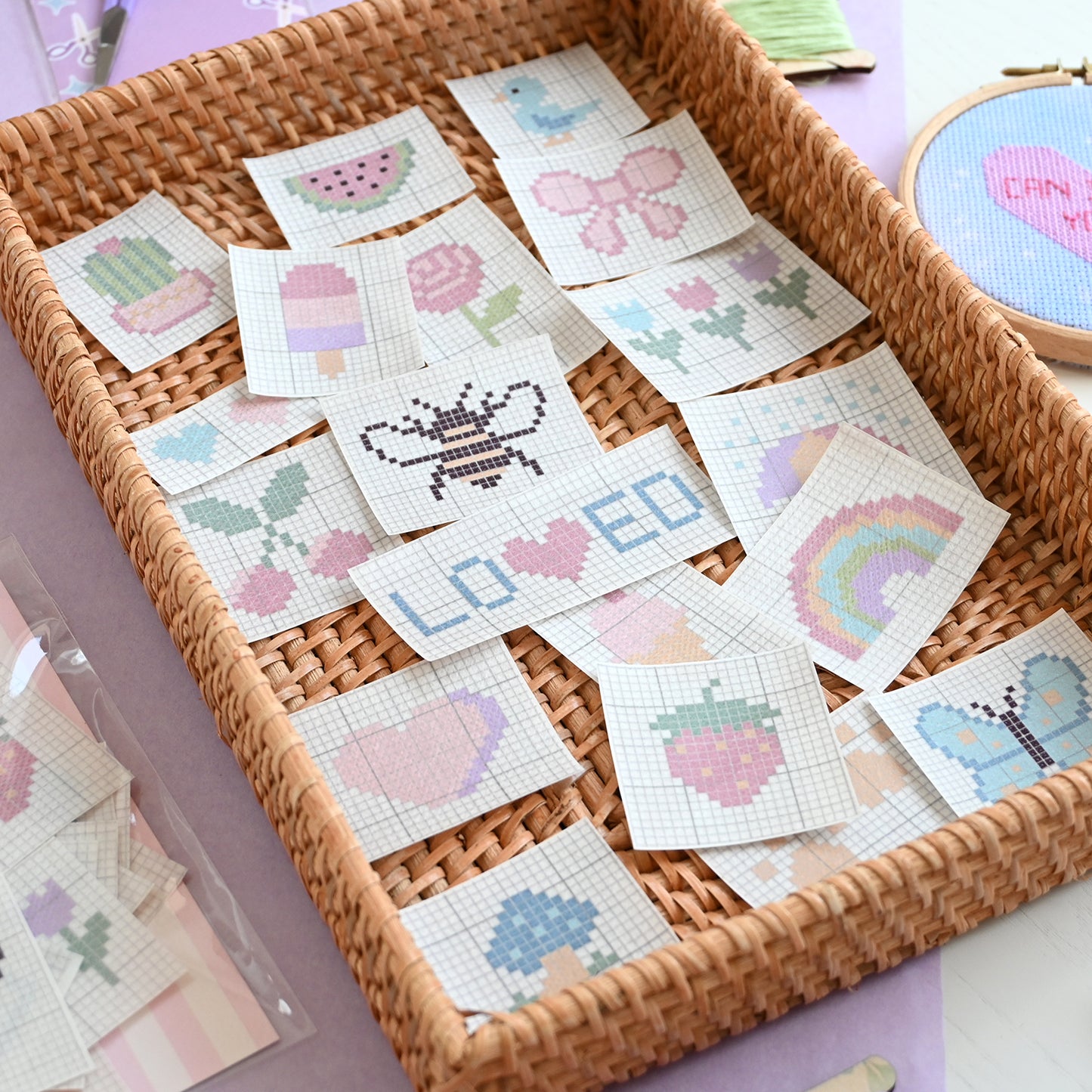 Cross-stitch pattern patches in a woven basket with embroidery hoop in the background