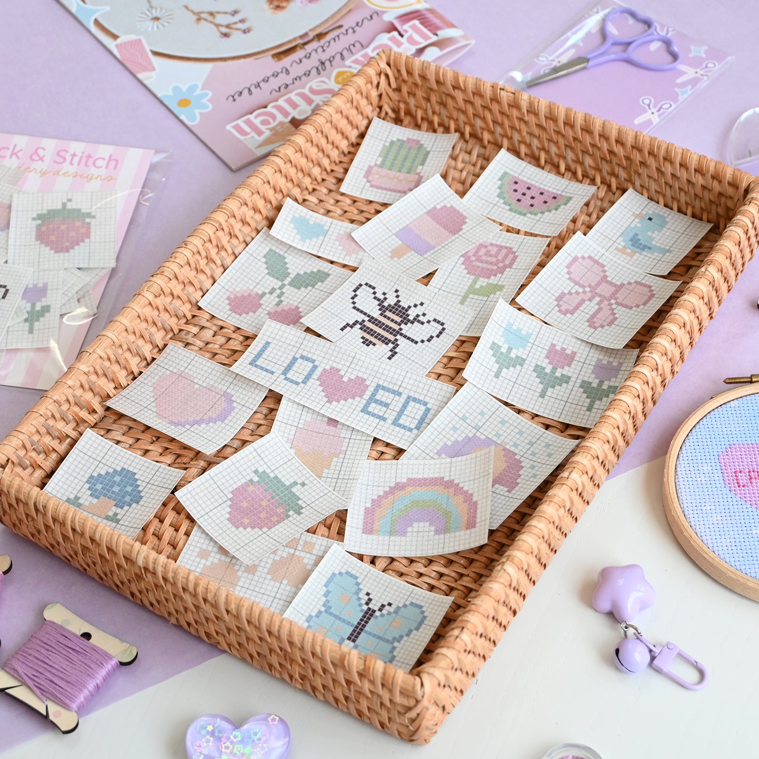 Cross-stitch patterns in a woven tray with embroidery tools on a light purple background