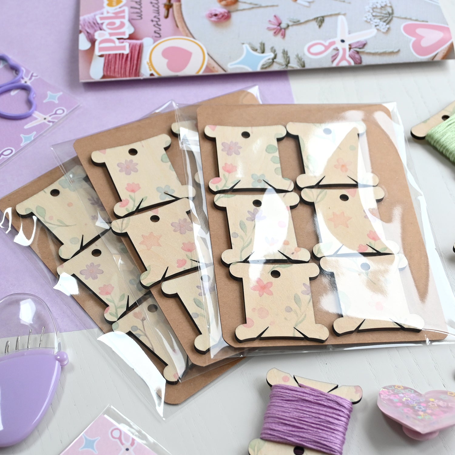 Wooden thread bobbins with floral patterns on a white surface with crafting supplies.